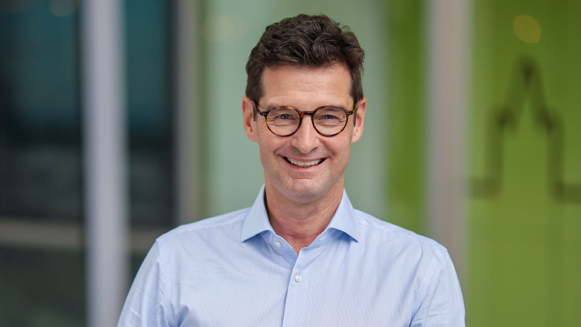 BIH-Vorstandsvorsitzender lehnt in einem hellblauen Oberhemd lächelnd an einem Stehtisch.